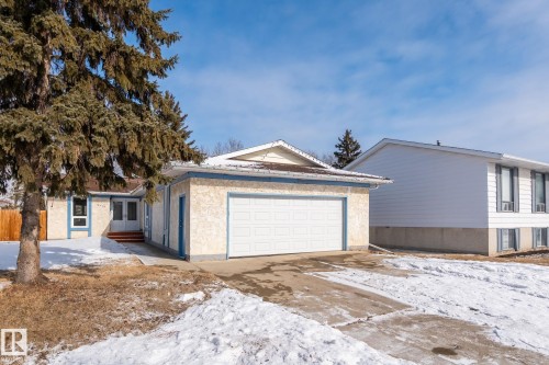 The property features an attached garage with a white door, a paved driveway, and an exterior with a cream stucco finish and blue trim - 18124 68Ave, Edmonton, AB - Outdoor
