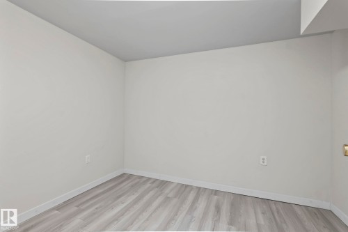 This room features light grey walls, light-toned wood plank flooring, and white baseboards - 18124 68Ave, Edmonton, AB - Indoor Photo Showing Other Room