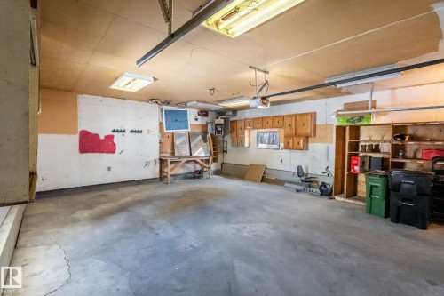 The property features a spacious garage with a concrete floor, built-in wooden cabinetry, and overhead fluorescent lighting - 18124 68Ave, Edmonton, AB - Indoor Photo Showing Garage