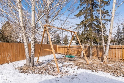 The property features a fenced backyard with mature trees and a wooden swing set - 18124 68Ave, Edmonton, AB - Outdoor