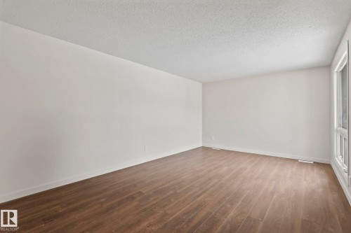 Spacious room featuring wood-look flooring, white walls, and a large window providing natural light - 18124 68Ave, Edmonton, AB - Indoor Photo Showing Other Room