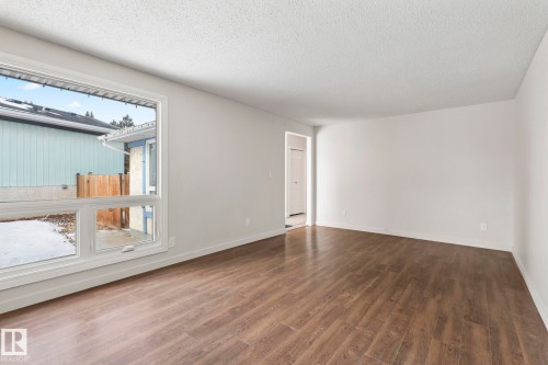 This bright room features a large window with white trim, wood-style flooring, and light-colored walls - 18124 68Ave, Edmonton, AB - Indoor Photo Showing Other Room