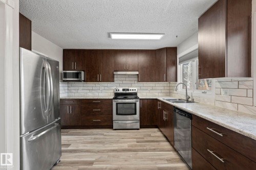 The kitchen features dark wood cabinetry, a white subway tile backsplash, and light-colored countertops - 18124 68Ave, Edmonton, AB - Indoor Photo Showing Kitchen With Double Sink With Upgraded Kitchen