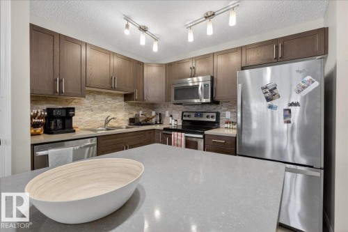 Well-appointed kitchen featuring abundant cabinetry, stainless steel appliances, a tiled backsplash, and a spacious countertop - 33 4029 Orchards Drive Sw, Edmonton, AB - Indoor Photo Showing Kitchen With Double Sink