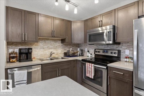 The kitchen features dark wood cabinetry, a light-colored countertop, and a tiled backsplash - 33 4029 Orchards Drive Sw, Edmonton, AB - Indoor Photo Showing Kitchen With Double Sink With Upgraded Kitchen