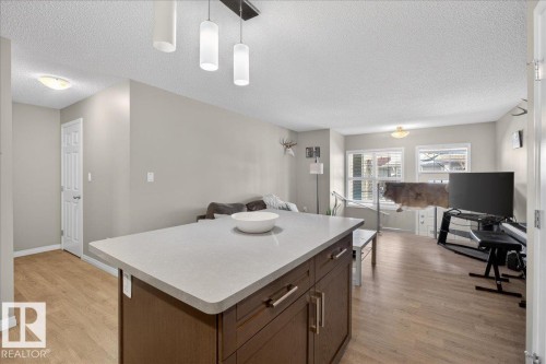 Open concept living area featuring light wood flooring, a kitchen island with a light-colored countertop, and a living room with windows providing natural light - 33 4029 Orchards Drive Sw, Edmonton, AB - Indoor