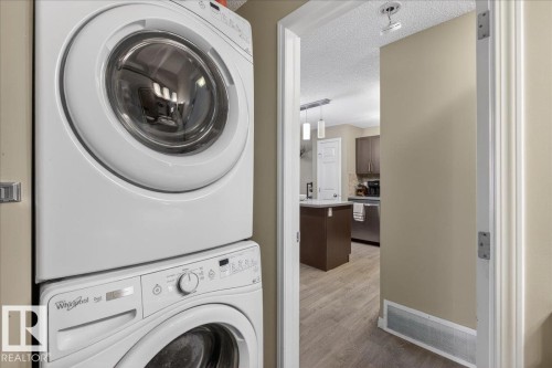 Laundry area with a stacked washer and dryer, located near an entryway leading into the kitchen - 33 4029 Orchards Drive Sw, Edmonton, AB - Indoor Photo Showing Laundry Room