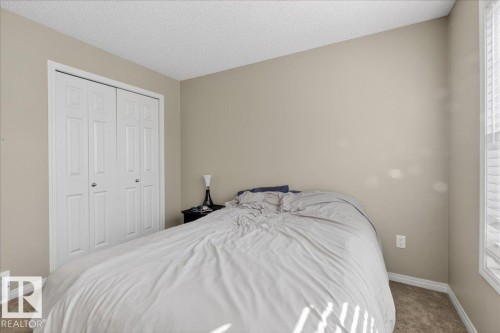 This property features a room with light-colored walls and carpeting, a window with horizontal blinds, and a closet with bifold doors - 33 4029 Orchards Drive Sw, Edmonton, AB - Indoor Photo Showing Bedroom