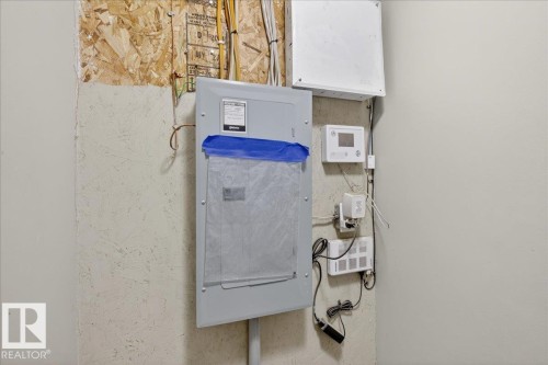 The property features an electrical panel and various utility boxes mounted on the wall, with exposed wiring and a wood panel section - 33 4029 Orchards Drive Sw, Edmonton, AB - Indoor