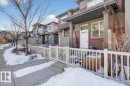 The property features a private fenced patio area, a white front door with an overhead transom window, and red siding on the exterior - 33 4029 Orchards Drive Sw, Edmonton, AB  - Outdoor 