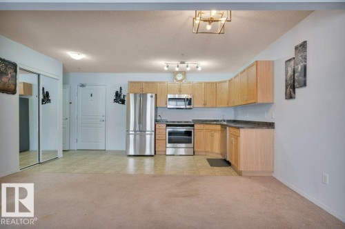 Open concept living area featuring a kitchen with light wood cabinetry, stainless steel appliances, and dark countertops - 103 309 Clareview Station Drive, Edmonton, AB - Indoor Photo Showing Kitchen
