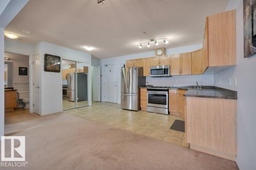 Kitchen featuring wood cabinetry, stainless steel appliances, and a tiled floor - 103 309 Clareview Station Drive, Edmonton, AB - Indoor Photo Showing Kitchen