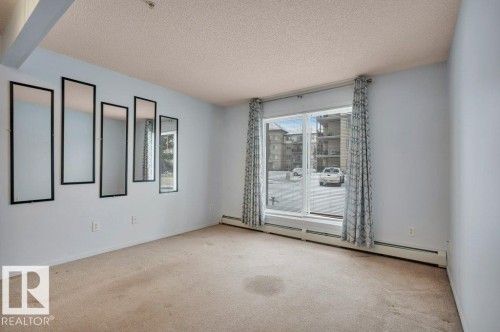 This spacious room features light-colored carpeting, light blue walls, and a large window with patterned curtains providing views of the exterior - 103 309 Clareview Station Drive, Edmonton, AB - Indoor Photo Showing Other Room