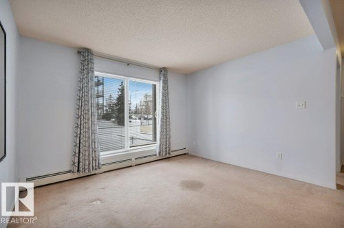 Living area featuring wall-to-wall carpeting and sliding glass doors with patterned curtains - 103 309 Clareview Station Drive, Edmonton, AB - Indoor Photo Showing Other Room