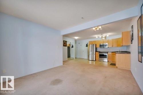 Open concept living space featuring a kitchen with stainless steel appliances, light wood cabinetry, and a carpeted floor in the main area - 103 309 Clareview Station Drive, Edmonton, AB - Indoor Photo Showing Kitchen