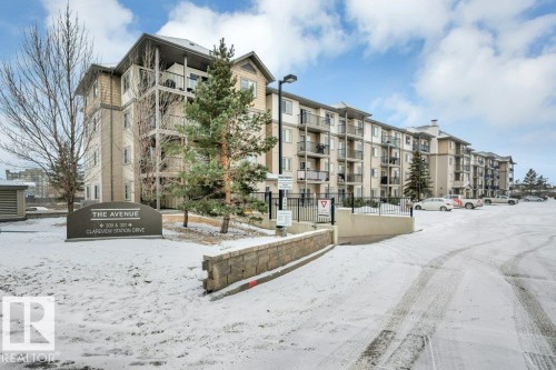The property features a multi-story building with balconies, a paved parking area, and a stone-faced retaining wall - 103 309 Clareview Station Drive, Edmonton, AB - Outdoor With Facade