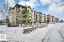 The property features a multi-story building with balconies, a paved parking area, and a stone-faced retaining wall - 103 309 Clareview Station Drive, Edmonton, AB  - Outdoor With Facade 