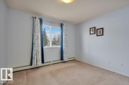 This room features a window with blue and white patterned curtains, light-colored walls, and carpeting - 103 309 Clareview Station Drive, Edmonton, AB - Indoor Photo Showing Other Room