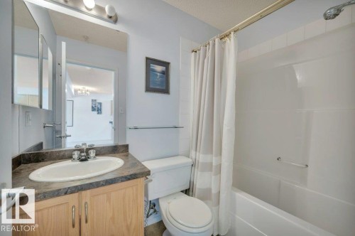 The bathroom features a light-colored vanity with a built-in sink, a wall-mounted mirror, and a full-sized bathtub with a shower - 103 309 Clareview Station Drive, Edmonton, AB - Indoor Photo Showing Bathroom