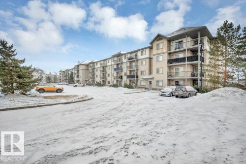 The property features a multi-story building with balconies and a paved parking area - 103 309 Clareview Station Drive, Edmonton, AB - Outdoor With Balcony With Facade