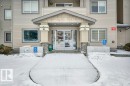 The property features a building exterior with light-colored siding, a covered entrance with stone accent pillars, and large glass doors - 103 309 Clareview Station Drive, Edmonton, AB  - Outdoor With Facade 