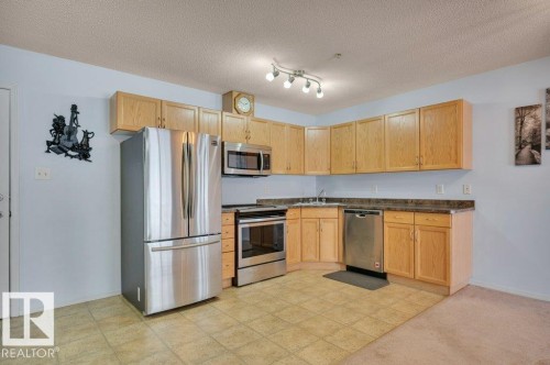 The kitchen features light-colored cabinetry, stainless steel appliances including a refrigerator, oven, microwave, and dishwasher, and a tiled floor - 103 309 Clareview Station Drive, Edmonton, AB - Indoor Photo Showing Kitchen
