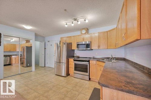 The kitchen features stainless steel appliances, wood cabinetry, a double basin sink, and ample countertop space - 103 309 Clareview Station Drive, Edmonton, AB - Indoor Photo Showing Kitchen With Double Sink