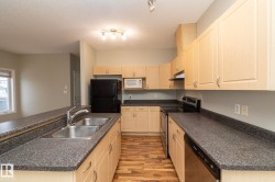 Kitchen with appliances with stainless steel finishes, dark countertops, light wood-type flooring, an island with sink, and under cabinet range hood - 