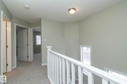 Corridor featuring an upstairs landing, a textured ceiling, and light carpet - 