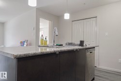 Kitchen featuring an island with sink, light countertops, stainless steel dishwasher, and dark wood-style floors - 