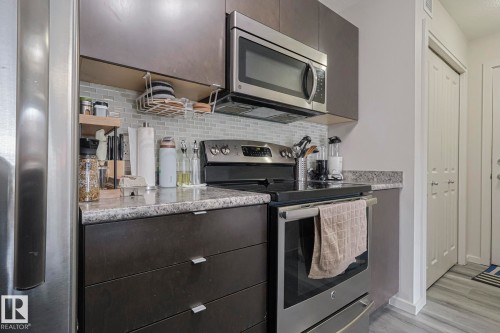 Kitchen featuring stainless steel appliances, dark wood finish cabinets, tasteful backsplash, light wood-style floors, and modern cabinets - 236 344 Windermere Road, Edmonton, AB - Indoor Photo Showing Kitchen With Stainless Steel Kitchen With Upgraded Kitchen