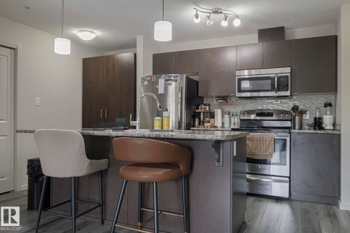 Kitchen featuring stainless steel appliances, a kitchen breakfast bar, decorative light fixtures, an island with sink, and dark wood finish cabinets - 236 344 Windermere Road, Edmonton, AB - Indoor Photo Showing Kitchen With Stainless Steel Kitchen With Upgraded Kitchen