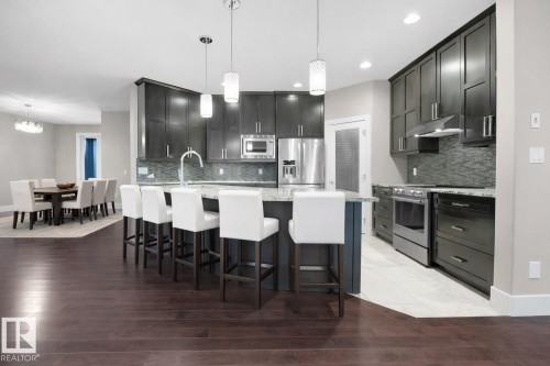 Kitchen with stainless steel appliances, a kitchen breakfast bar, light stone countertops, dark wood-style floors, and recessed lighting - 59 10550 Ellerslie Road, Edmonton, AB - Indoor Photo Showing Kitchen With Upgraded Kitchen