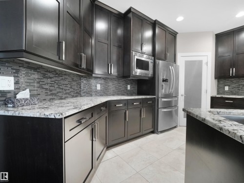 Kitchen with appliances with stainless steel finishes, decorative backsplash, light stone countertops, recessed lighting, and light tile patterned floors - 59 10550 Ellerslie Road, Edmonton, AB - Indoor Photo Showing Kitchen With Upgraded Kitchen