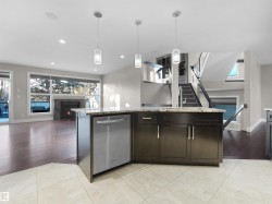 Kitchen featuring open floor plan, hanging light fixtures, stainless steel dishwasher, light stone counters, and a lit fireplace - 