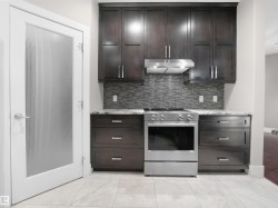Kitchen with stainless steel gas range oven, dark brown cabinets, light stone countertops, and under cabinet range hood - 