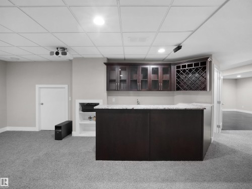 Bar with dark brown cabinets, glass insert cabinets, light carpet, recessed lighting, and light stone countertops - 59 10550 Ellerslie Road, Edmonton, AB - Indoor Photo Showing Other Room