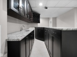 Kitchen featuring dark cabinetry, glass insert cabinets, and light stone countertops - 