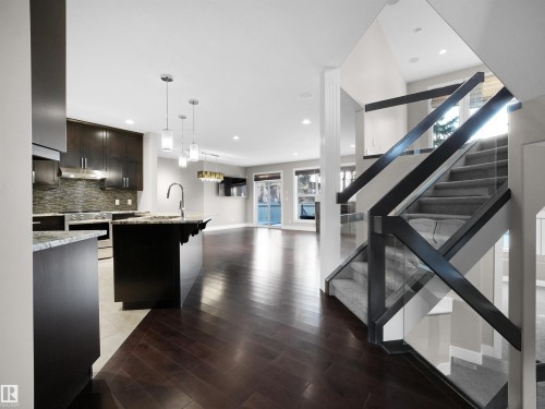 Kitchen featuring open floor plan, hanging light fixtures, stainless steel stove, dark wood-style flooring, and dark brown cabinetry - 59 10550 Ellerslie Road, Edmonton, AB - Indoor Photo Showing Kitchen With Upgraded Kitchen