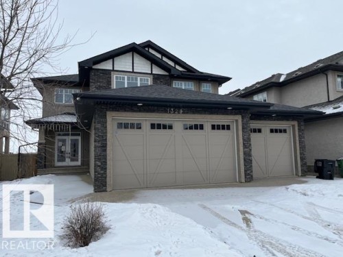 The property features a two-story exterior with a combination of stucco and stone accents, a dark shingled roof, and a prominent double garage with carriage-style doors - 1328 Adamson Drive, Edmonton, AB - Outdoor