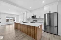 Kitchen with stainless steel appliances, an island with sink, backsplash, white cabinetry, and light wood-style floors - 