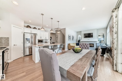 Open concept interior featuring hardwood floors, a kitchen with stainless steel appliances and white cabinetry, a dining area with a wooden table, and a living area with a fireplace - 11 Etoile Cres N, St. Albert, AB - Indoor