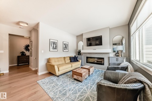Living area featuring hardwood floors, a fireplace with a light-colored brick surround, and large windows providing natural light - 11 Etoile Cres N, St. Albert, AB - Indoor Photo Showing Living Room With Fireplace