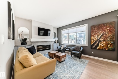 The living area features light wood flooring, a fireplace with a light-colored tile surround, and a large window providing natural light - 11 Etoile Cres N, St. Albert, AB - Indoor Photo Showing Living Room With Fireplace