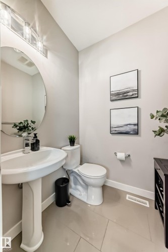 The bathroom features a pedestal sink, a circular mirror with contemporary lighting, and tiled flooring - 11 Etoile Cres N, St. Albert, AB - Indoor Photo Showing Bathroom