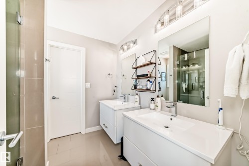Well-appointed bathroom featuring two modern vanities with integrated sinks, large mirrors, and contemporary light fixtures - 11 Etoile Cres N, St. Albert, AB - Indoor Photo Showing Bathroom