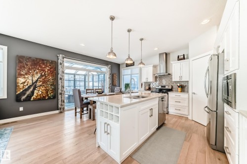 Open-concept kitchen and dining area featuring light-toned hardwood flooring, white cabinetry, a kitchen island with a light-colored countertop, and stainless steel appliances - 11 Etoile Cres N, St. Albert, AB - Indoor Photo Showing Kitchen With Double Sink With Upgraded Kitchen