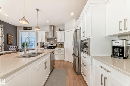 The kitchen features white cabinetry, a large island with a double sink, stainless steel appliances, and light-colored countertops - 11 Etoile Cres N, St. Albert, AB - Indoor Photo Showing Kitchen With Stainless Steel Kitchen With Double Sink With Upgraded Kitchen