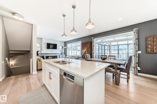 The open concept kitchen features an island with a double basin sink and a built-in dishwasher, illuminated by three pendant lights - 11 Etoile Cres N, St. Albert, AB - Indoor Photo Showing Kitchen With Double Sink