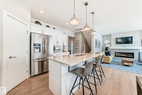 The property features an open-concept living area with hardwood flooring, a kitchen island with seating, pendant lighting, and stainless steel appliances - 11 Etoile Cres N, St. Albert, AB - Indoor Photo Showing Kitchen With Fireplace With Stainless Steel Kitchen With Double Sink With Upgraded Kitchen